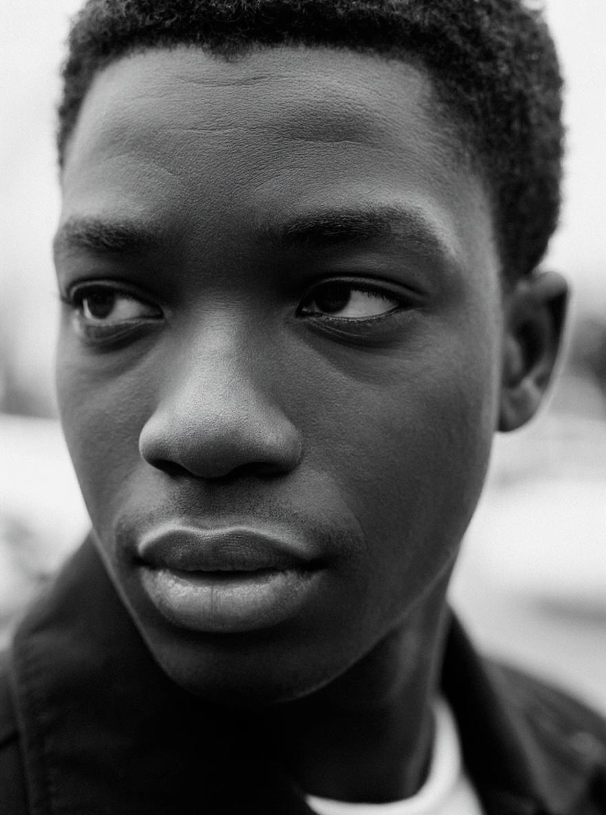 Black‑and‑white close‑up portrait, subject looking left with soft, blurred background.